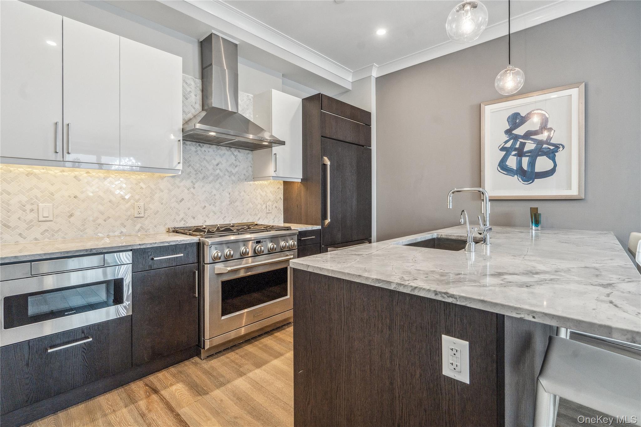 100 Garvies Point Road, Unit 1126 Glen Cove, NY 11542 - Photo 22 of 40 Kitchen with high end appliances, sink, wall chimney range hood, white cabinets, and hanging light fixtures