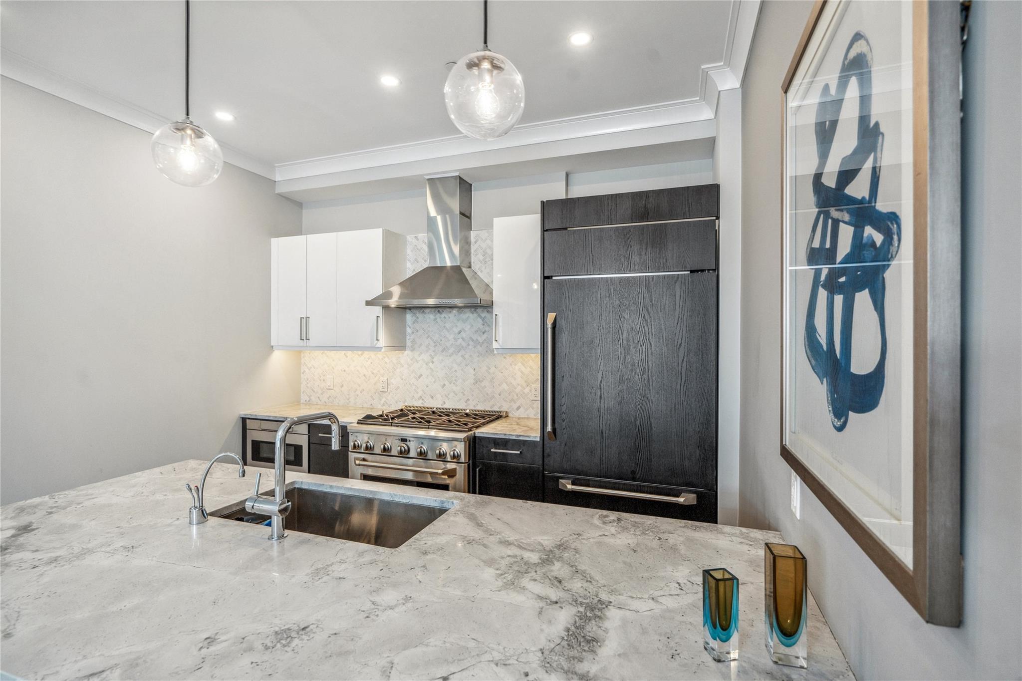100 Garvies Point Road, Unit 1126 Glen Cove, NY 11542 - Photo 24 of 40 Kitchen with premium appliances, sink, wall chimney range hood, white cabinets, and hanging light fixtures