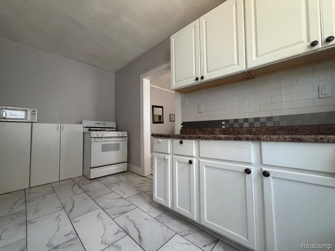9940 Manor Detroit, MI 48204 - Photo 11 of 16 Kitchen featuring white shaker-style cabinetry, dark speckled countertops, and a white subway tile backsplash with a checkered accent