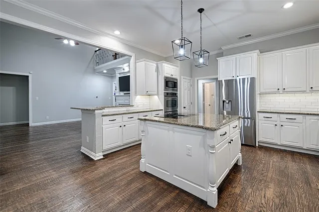 a kitchen with stainless steel appliances granite countertop a sink a stove a refrigerator and white cabinets with wooden floor