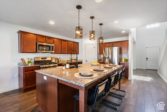 3456 South Linden Way Syracuse, UT 84075 - Photo 9 of 50 Kitchen featuring stainless steel appliances, an island with sink, light stone counters, dark wood-type flooring, and baseboards