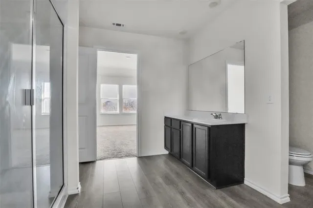 a view of an empty room with wooden floor and a bathroom
