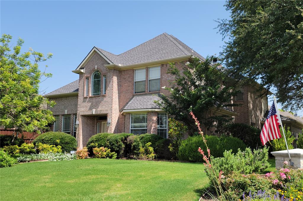 Brick facade residence featuring a prominent arched window, multi-gabled roofline, and established front landscaping