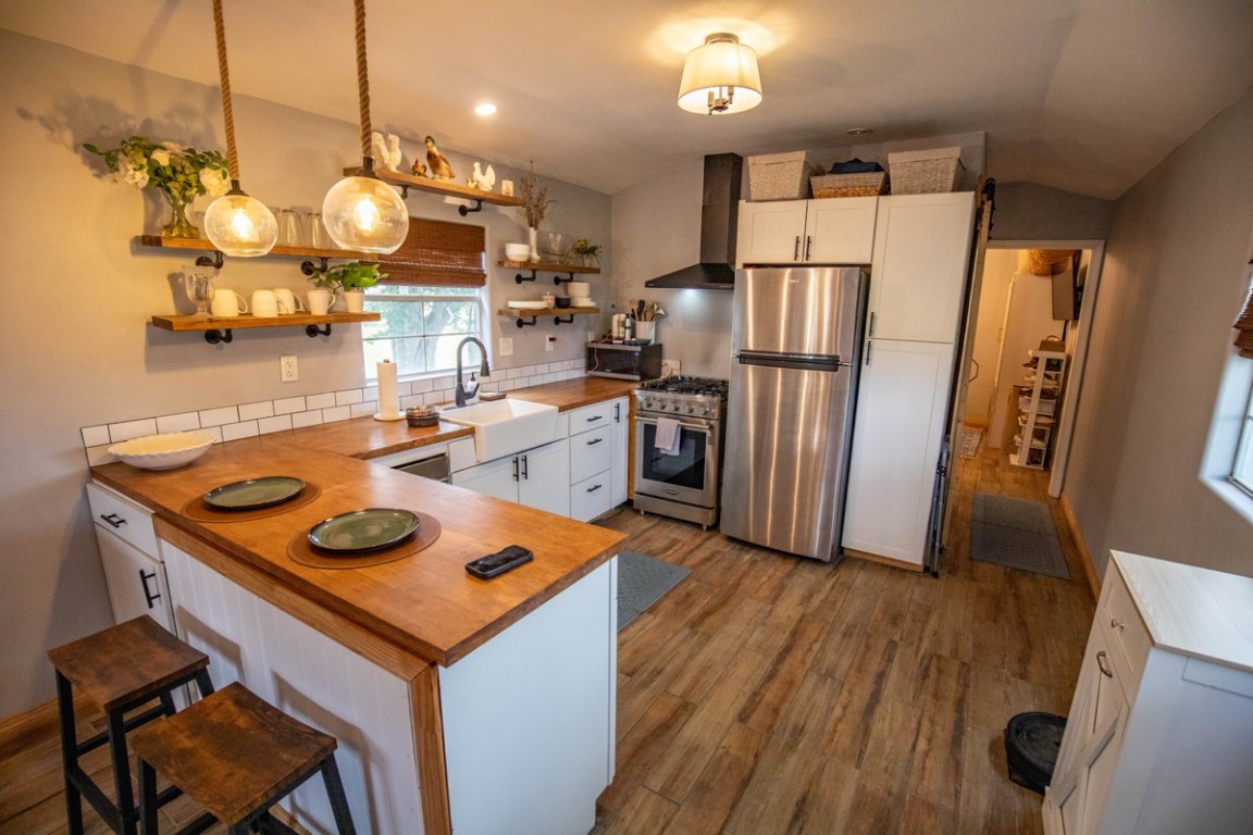 143 Harrison Road Beeville, TX 78102 - Photo 8 of 39 Kitchen with appliances with stainless steel finishes, butcher block countertops, wall chimney exhaust hood, open shelves, and a peninsula