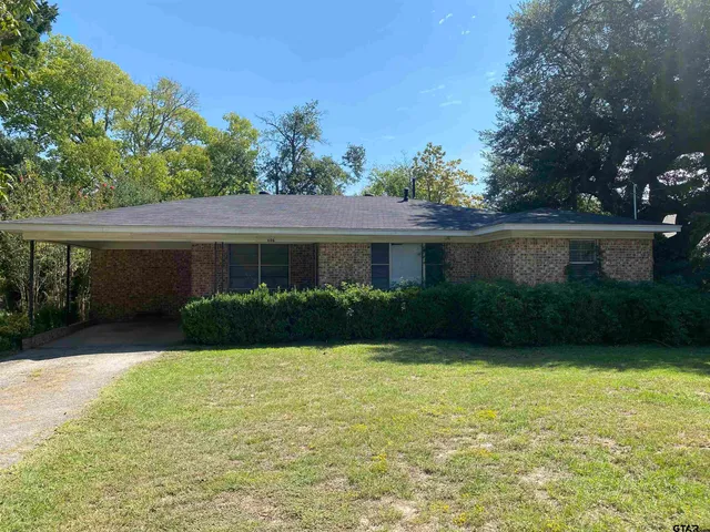 a view of a house next to a yard with potted plants and large trees