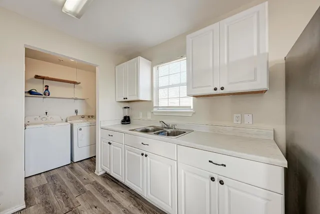 a kitchen with a sink dishwasher and white cabinets with wooden floor
