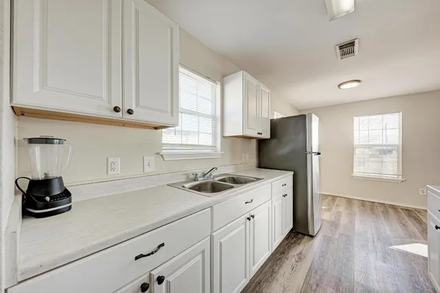 a kitchen with stainless steel appliances granite countertop a sink dishwasher a refrigerator and white cabinets with wooden floor