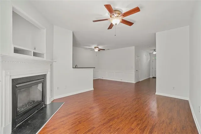 an empty room with wooden floor a ceiling fan a fireplace and windows