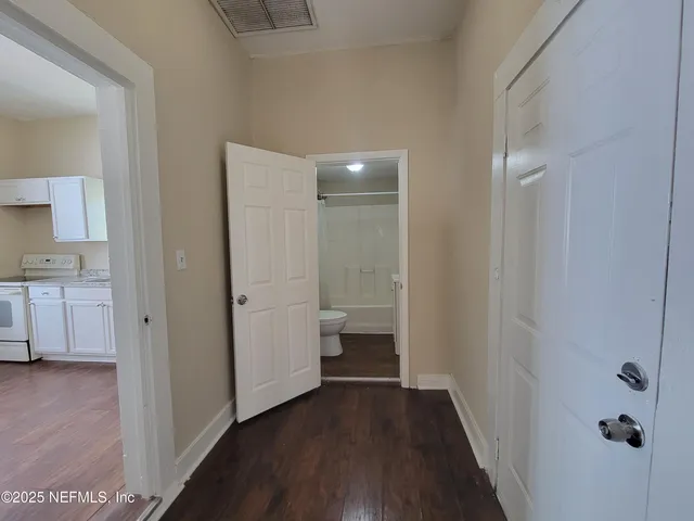 a view of a hallway with wooden floor and a bathroom