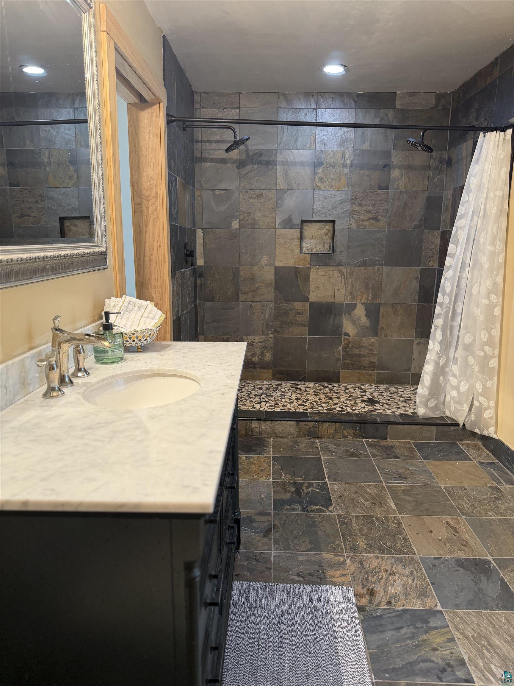 5274 Marble Lake Road Two Harbors, MN 55616 - Photo 32 of 79 Walk-in shower with dual shower heads, natural stone tile surround, and pebble stone base