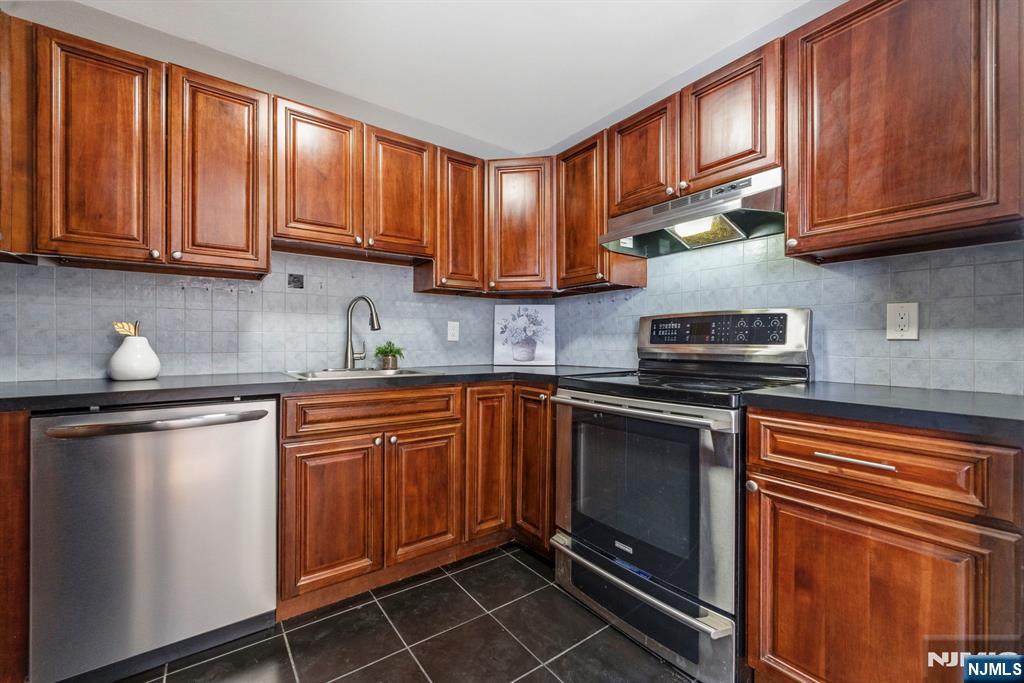 144 70th Street, Unit 1E Guttenberg, NJ 07093 - Photo 7 of 20 a kitchen with stainless steel appliances granite countertop wooden cabinets a stove top oven a sink and dishwasher
