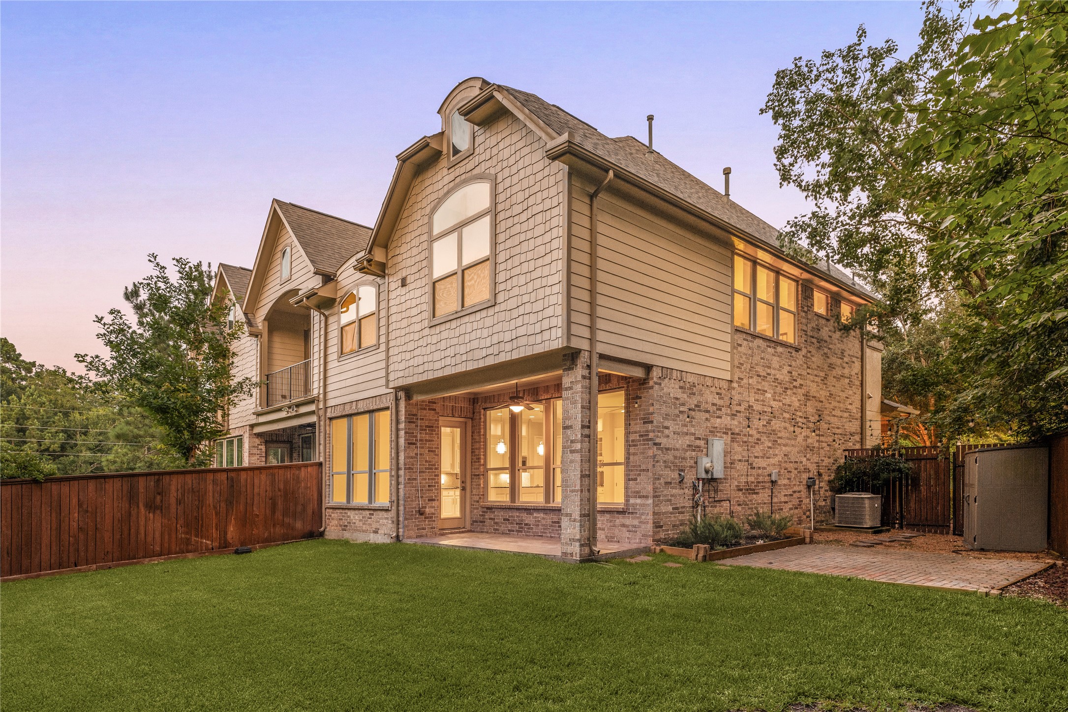 98 Herons Flight Place Spring, TX 77389 - Photo 20 of 29 Twilight view of the home's rear exterior, showcasing brick and shingle-style architecture, covered patio, and a private, fenced backyard.