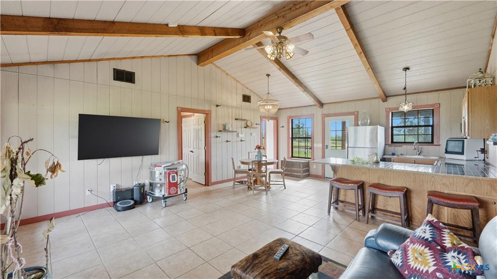 127 Offer Llano, TX 78643 - Photo 13 of 40 Open-concept living area featuring a vaulted ceiling with exposed wood beams, tile flooring, a kitchen island with seating, and a built-in kitchen sink