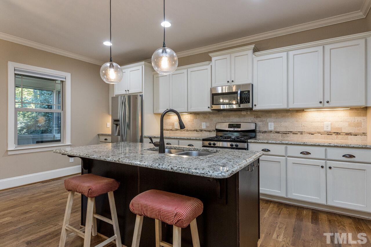 1340 Trinity Road Cary, NC 27513 - Photo 7 of 30 a kitchen with stainless steel appliances granite countertop a stove a sink dishwasher a microwave oven and a dining table with wooden floor