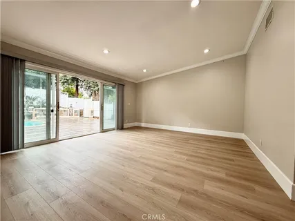 a view of an empty room with wooden floor and a kitchen