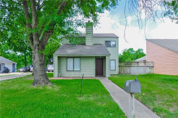a view of a yard in front of a house with plants and a large tree