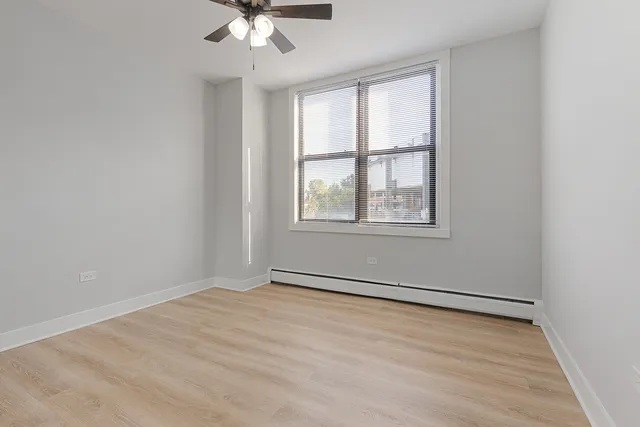 an empty room with wooden floor chandelier fan and windows