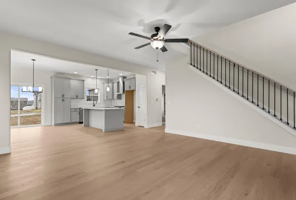 a view of an empty room with wooden floor and a kitchen