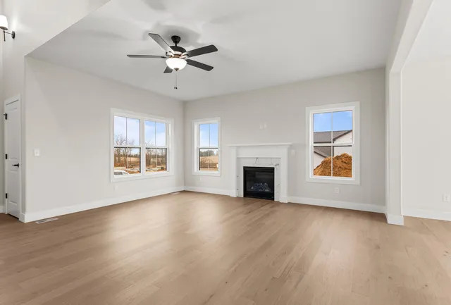 an empty room with wooden floor chandelier fan and windows