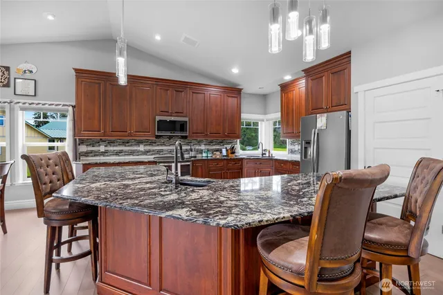 a kitchen with granite countertop kitchen island stainless steel appliances a table chairs sink refrigerator and microwave