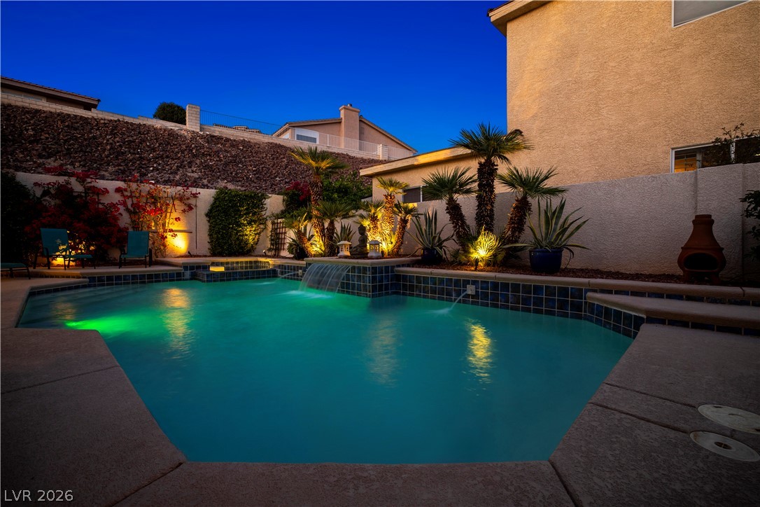 1135 Calico Ridge Drive Henderson, NV 89011 - Photo 72 of 86 An illuminated backyard oasis boasts a sparkling pool with elegant water features and lush landscaping.