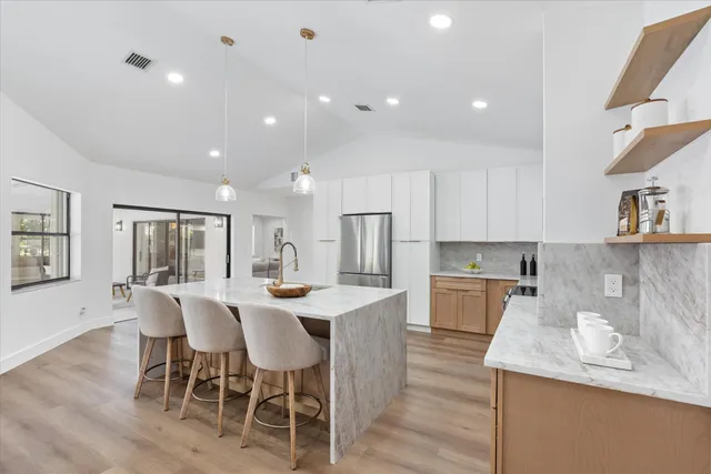 a large kitchen with stainless steel appliances a stove top oven a refrigerator a dining table and chairs with wooden floor