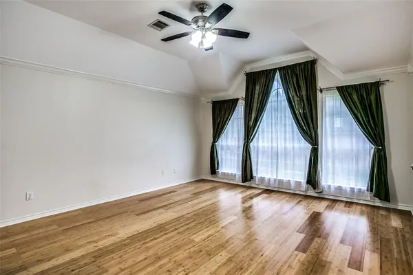 a view of an empty room with wooden floor and a ceiling fan