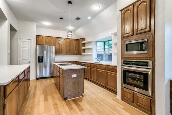 a kitchen with stainless steel appliances granite countertop a refrigerator a stove top oven a sink dishwasher and wooden cabinets with wooden floor