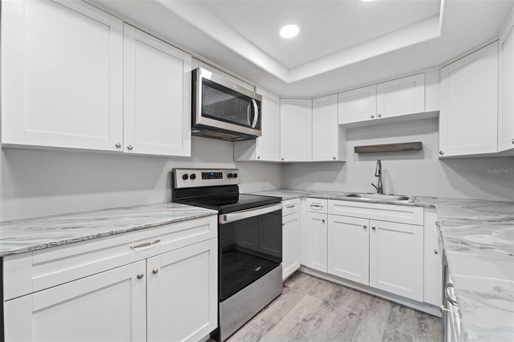 4238 Glissade Drive New Port Richey, FL 34652 - Photo 16 of 62 a kitchen with granite countertop white cabinets stainless steel appliances and a sink