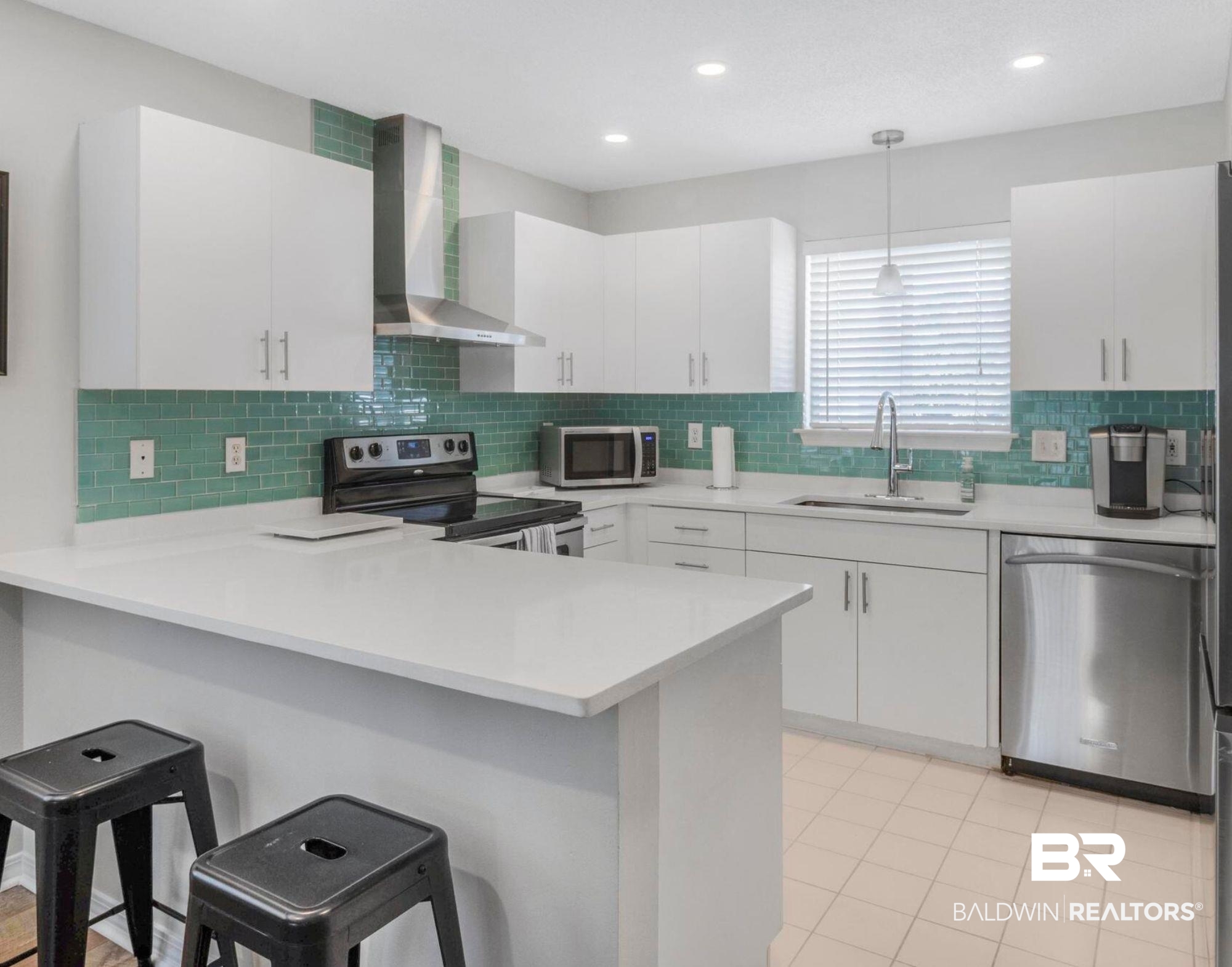 25957 Canal Road, Unit 306 Orange Beach, AL 36561 - Photo 7 of 28 Kitchen with a kitchen breakfast bar, white cabinetry, wall chimney exhaust hood, stainless steel appliances, and sink