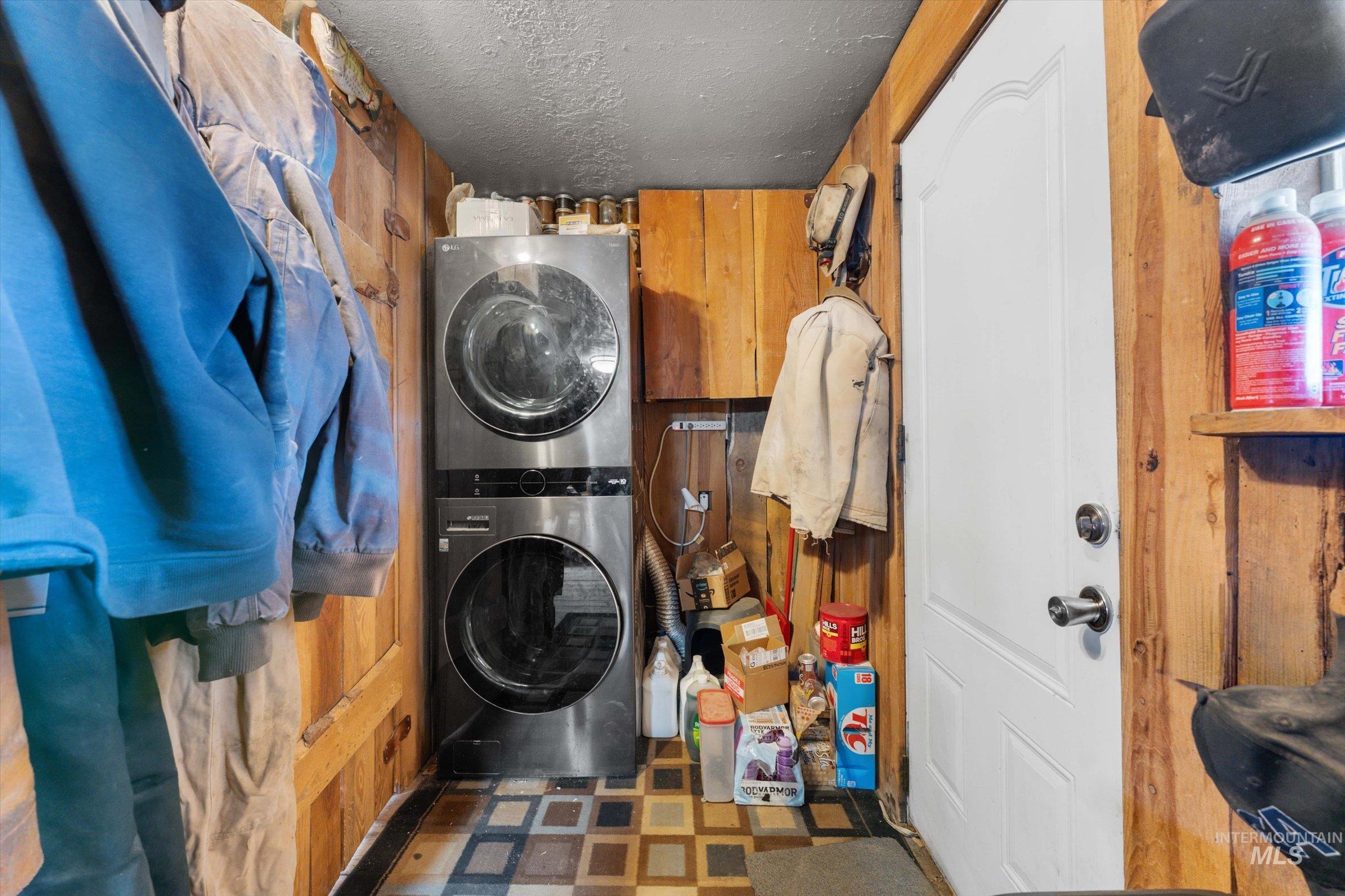 11555 Liberty Road Sweet, ID 83670 - Photo 27 of 49 Laundry area with dark flooring, a textured ceiling, stacked washing machine and dryer, and wooden walls