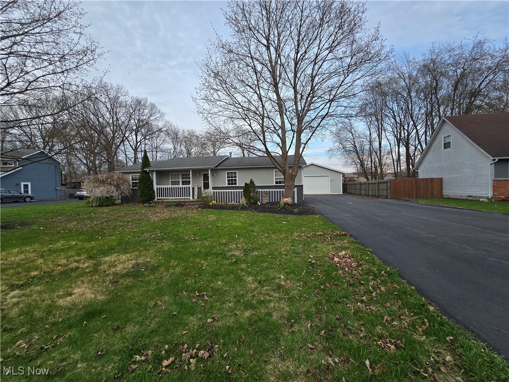 Ranch-style home with driveway, covered porch, fence, a garage, and a front yard