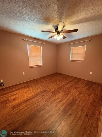 an empty room with wooden floor fan and windows