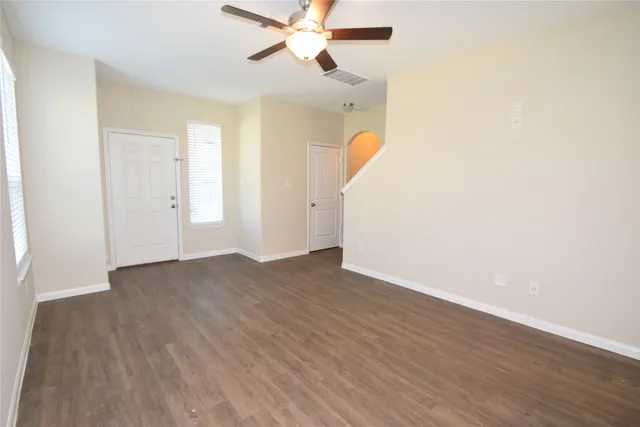 an empty room with wooden floor ceiling fan and windows