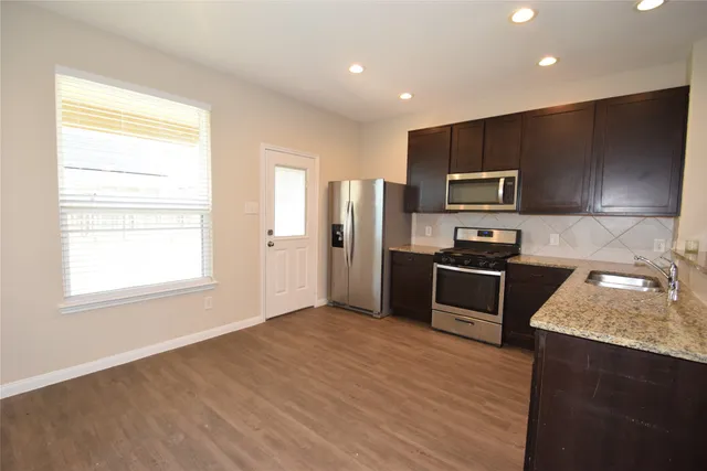 a kitchen with granite countertop stainless steel appliances a refrigerator cabinets and wooden floor