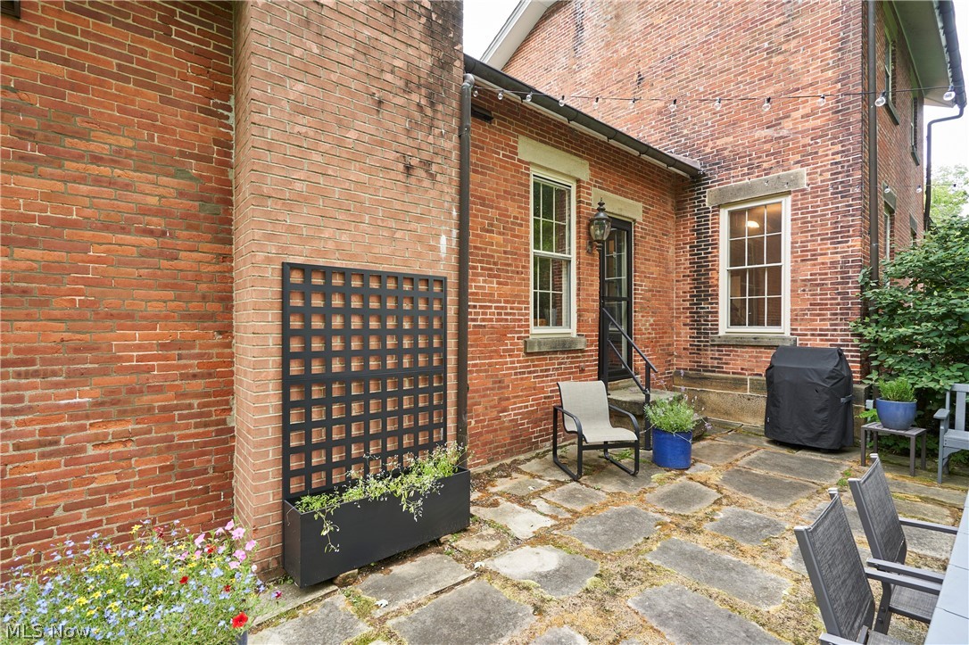 5046 Alger Road Richfield, OH 44286 - Photo 42 of 49 Brick exterior with a stone patio, featuring a black metal trellis planter, multiple windows with stone sills, and an exterior door with a lantern light fixture