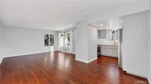 a view of empty room with wooden floor and kitchen