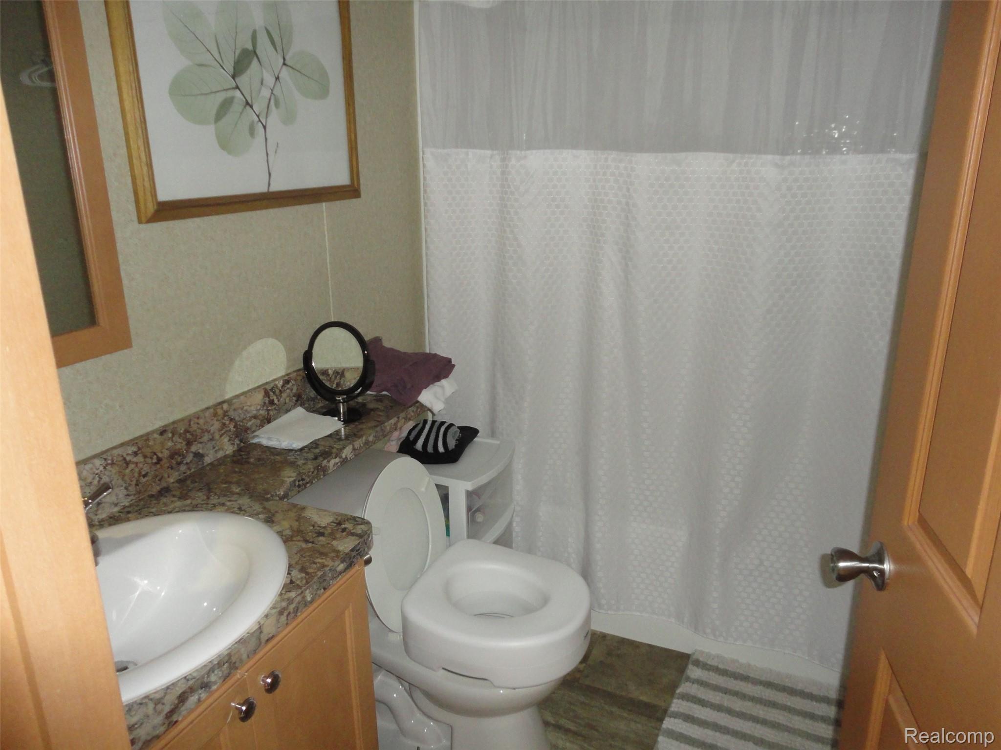 463 Edinborough Temperance, MI 48182 - Photo 12 of 23 Bathroom featuring a wood-finish vanity with a drop-in sink, a mottled countertop, and a shower with a privacy curtain
