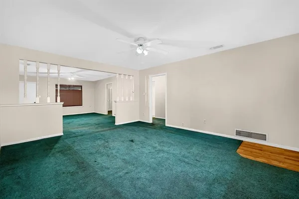 a view of an empty room with window and kitchen view