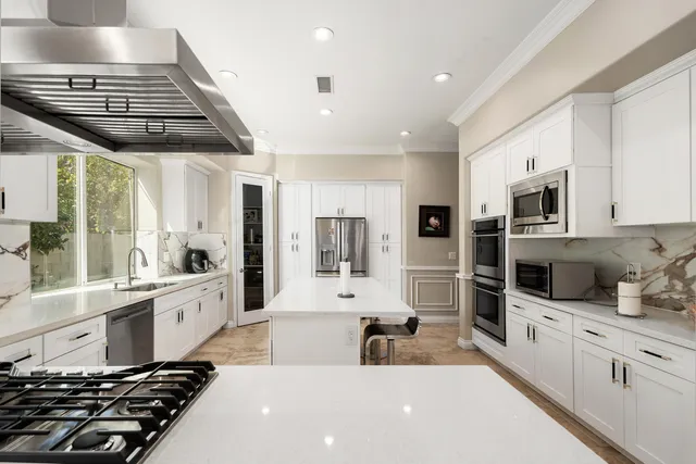 a large white kitchen with stainless steel appliances granite countertop a stove and a sink