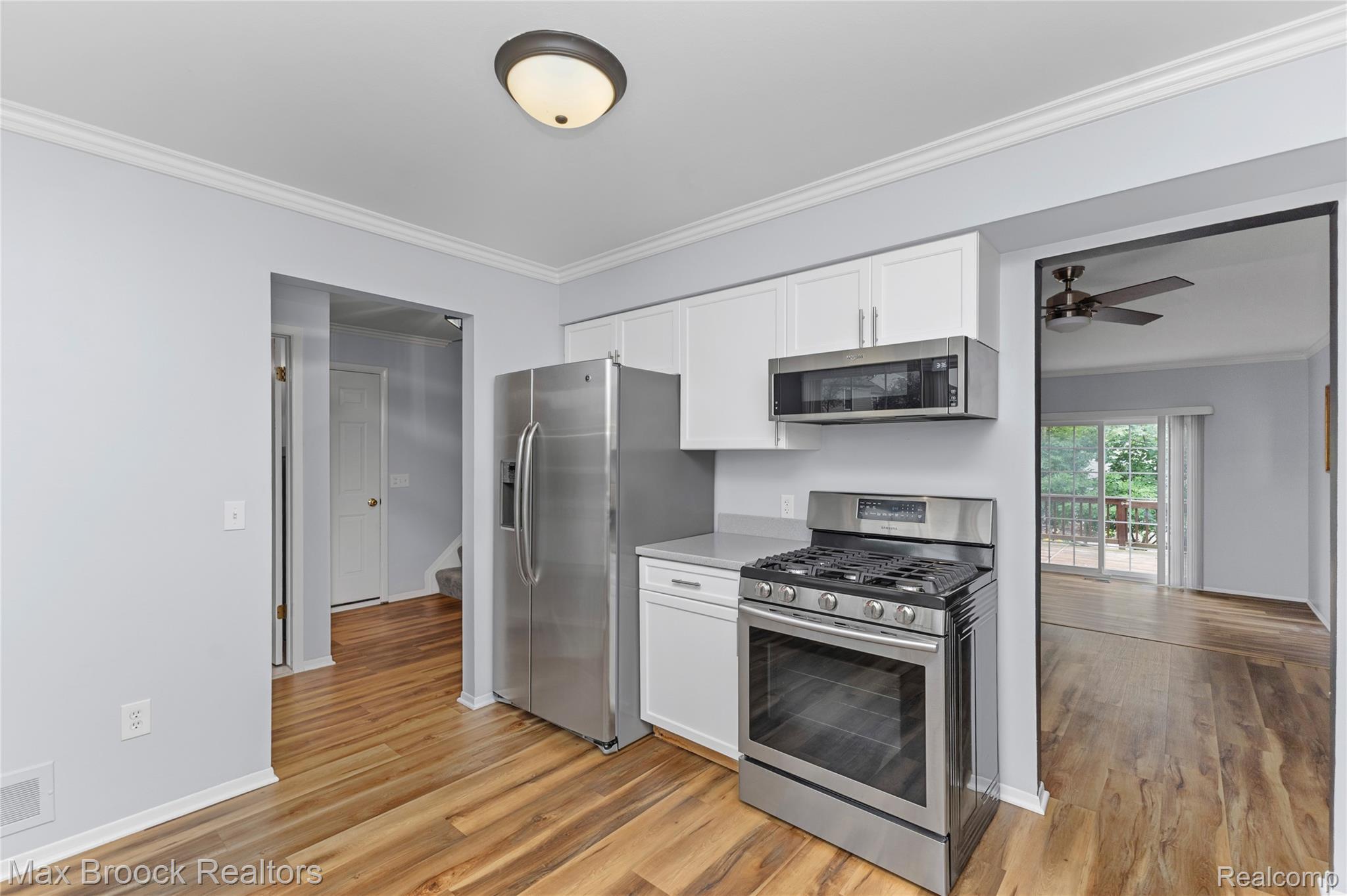 1157 Pine Ridge Court Rochester, MI 48306 - Photo 5 of 55 Updated kitchen featuring stainless steel gas range and built-in microwave, white cabinetry with chrome hardware, wood-finish flooring throughout, and stainless steel refrigerator with ample counter and storage space