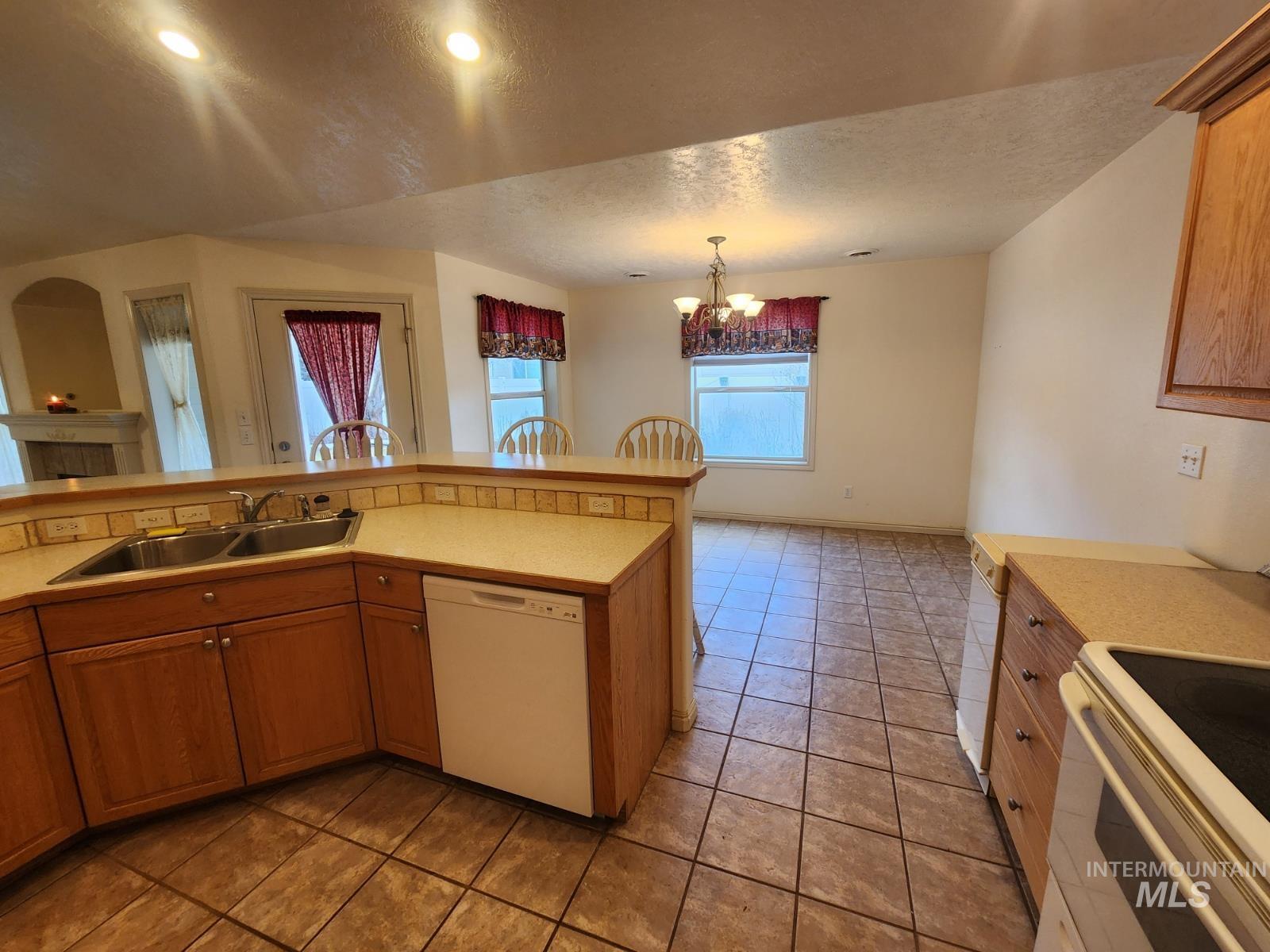 1000 North Rodeo Street Parma, ID 83660 - Photo 7 of 35 Kitchen featuring light countertops, white appliances, wood finish cabinets, a textured ceiling, and light tile patterned floors
