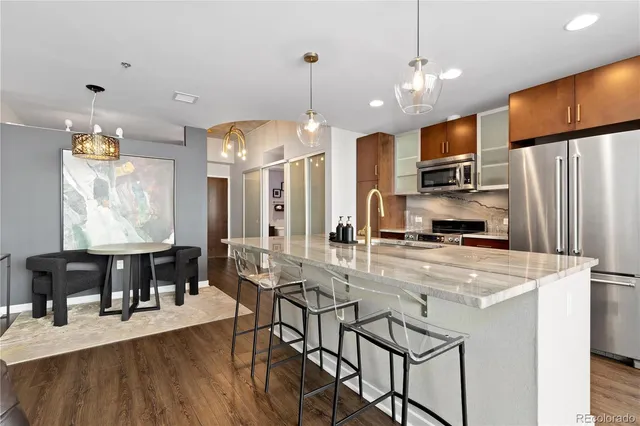 a kitchen with stainless steel appliances kitchen island granite countertop a refrigerator a stove a sink dishwasher and a dining table with wooden floor