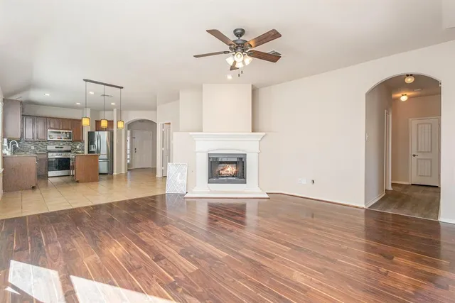 an empty room with wooden floor a ceiling fan a fireplace and windows
