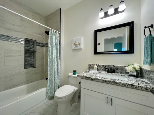 a bathroom with a granite countertop sink a toilet a mirror a vanity a bathtub and shower