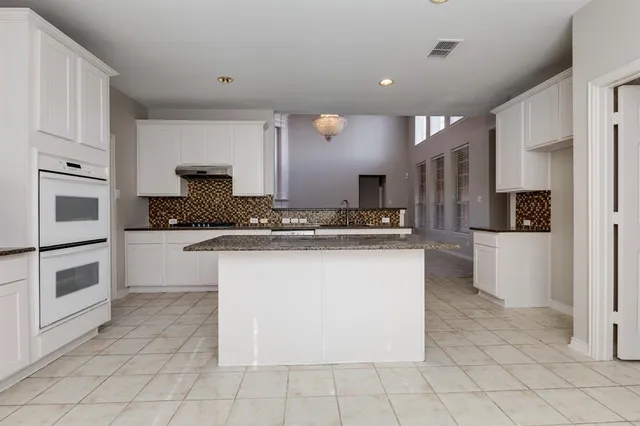 a kitchen with kitchen island granite countertop a stove a sink and white cabinets