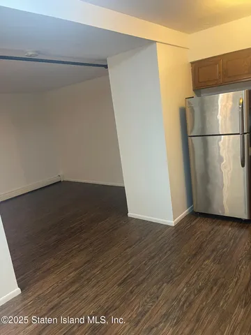 a view of a refrigerator in kitchen and an empty room with wooden floor