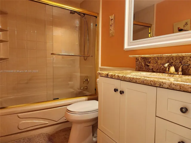 a bathroom with a granite countertop bathtub shower sink vanity and toilet