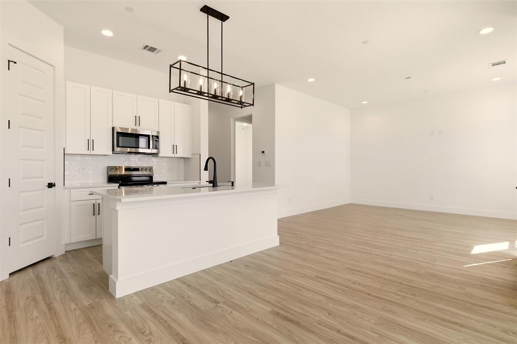 8902 Lowell Street Rowlett, TX 75089 - Photo 8 of 32 The property features an open-concept living space with light wood-style flooring, a kitchen island with a white countertop, and a kitchen equipped with stainless steel appliances