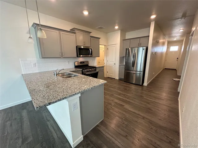 a kitchen with kitchen island granite countertop a stove top oven a sink dishwasher a refrigerator and microwave with wooden floor